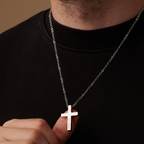 Person wearing a necklace with a cross pendant on a plain background