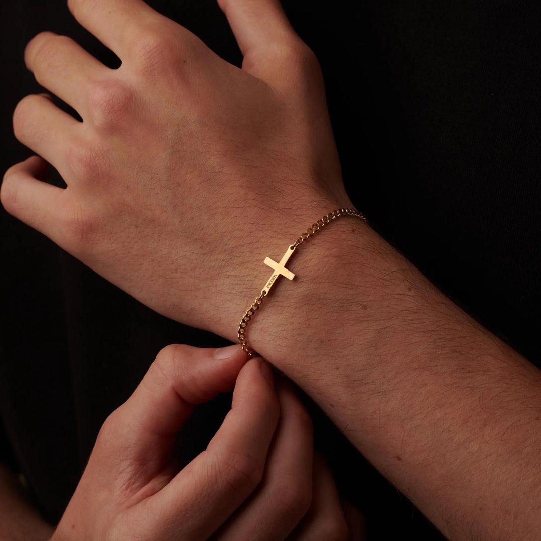 A close-up image of a person's hand wearing a gold cross-shaped bracelet.