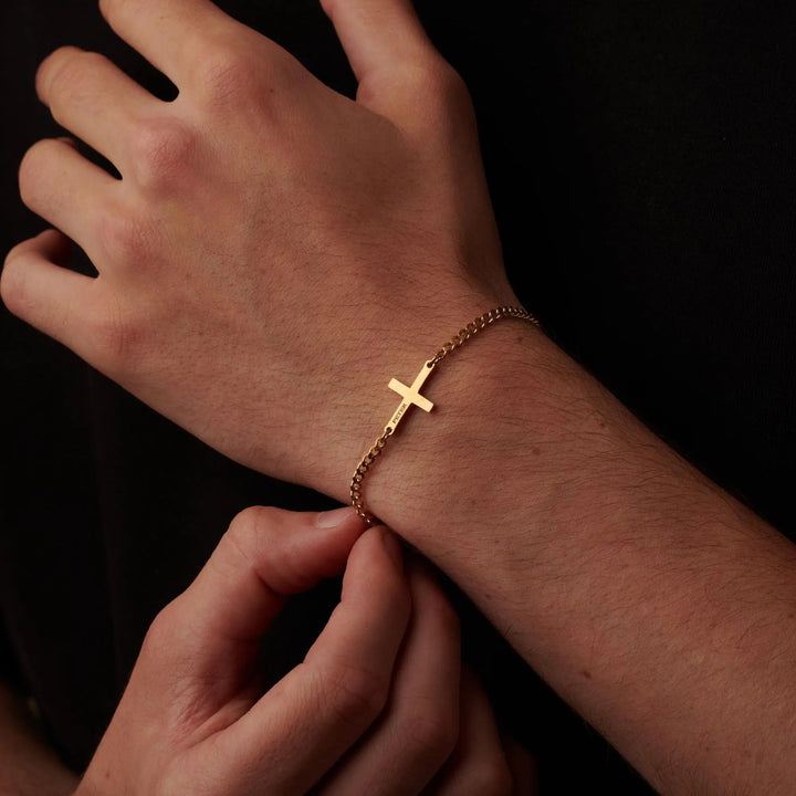 A close-up image of a person's hand wearing a gold cross-shaped bracelet.