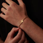 A close-up image of a person's hand wearing a gold cross-shaped bracelet.