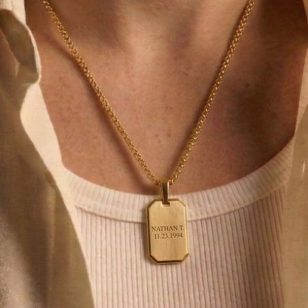 A gold-colored necklace with a rectangular pendant engraved with the name "Nathan T" and the date "11.23.1994".