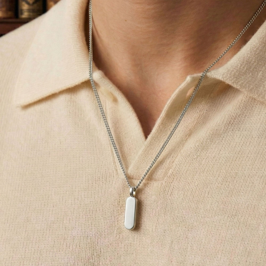 A silver necklace with a rectangular pendant is worn around a person's neck.