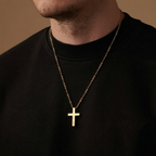 Gold cross necklace on a person wearing a black shirt against a brown background