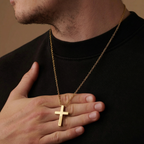 Man wearing a gold necklace with a cross pendant, holding it close to his chest.