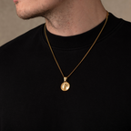 Gold necklace with a pendant on a person wearing a black shirt against a neutral background