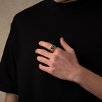 Person wearing a black t-shirt with a hand holding a gold ring featuring a black gemstone.