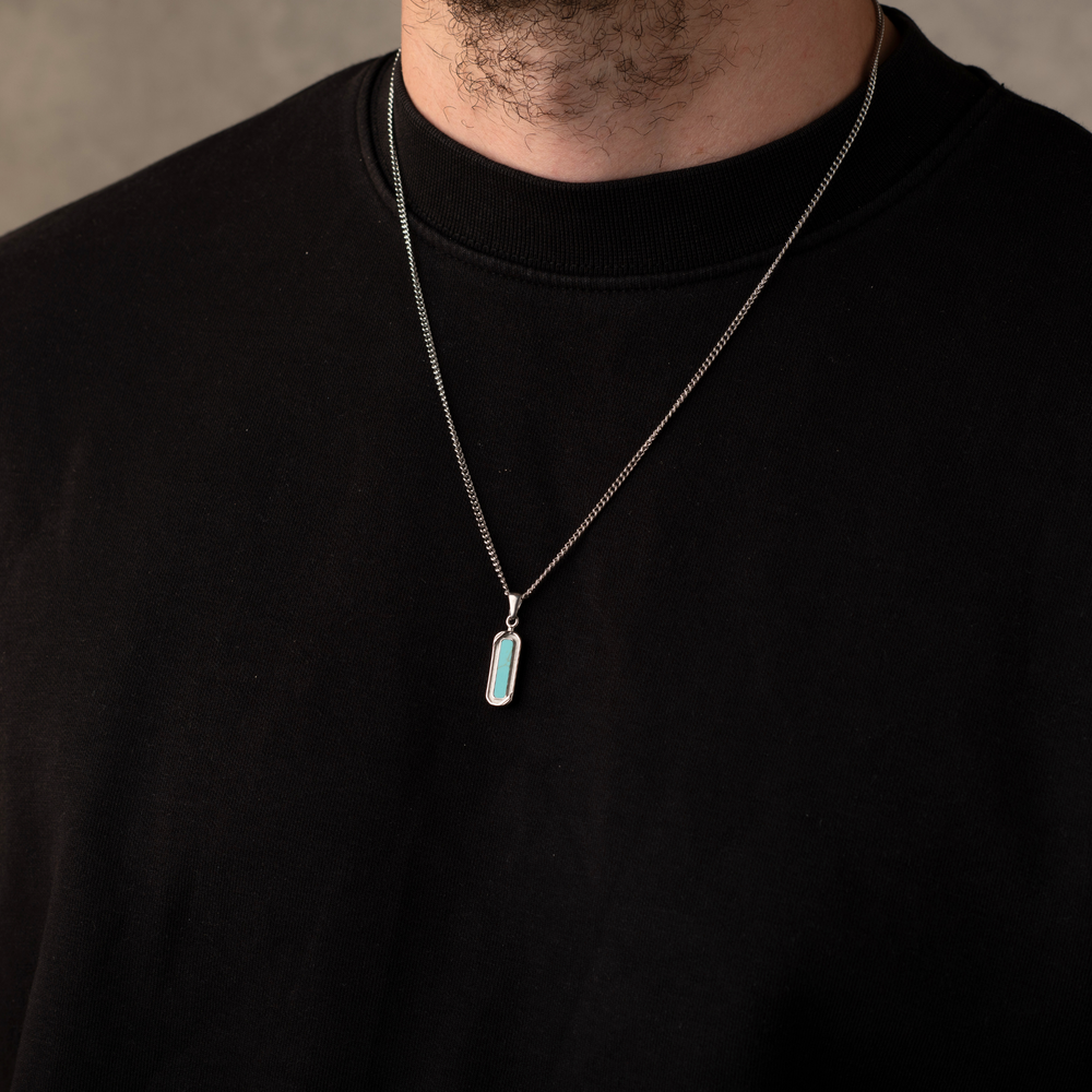 Person wearing a black shirt with a silver necklace featuring a turquoise pendant.