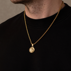Gold necklace with a pendant on a person wearing a black shirt against a neutral background
