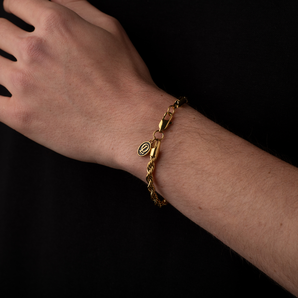 Gold bracelet on a wrist against a black background