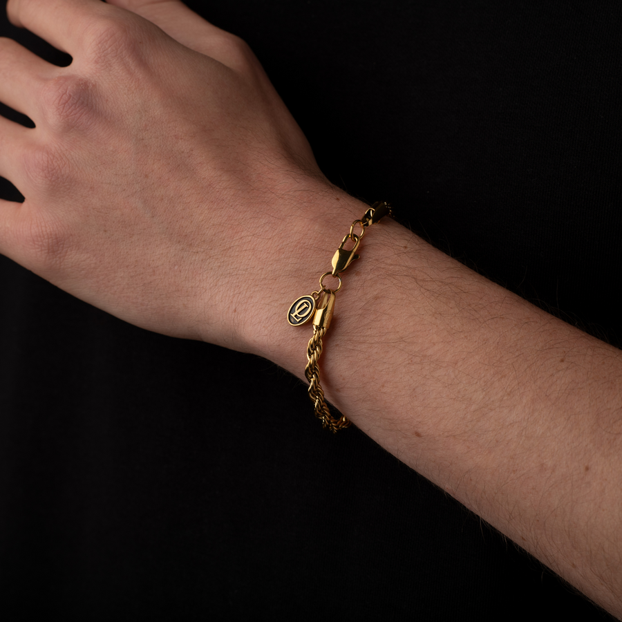 Gold bracelet on a wrist against a black background