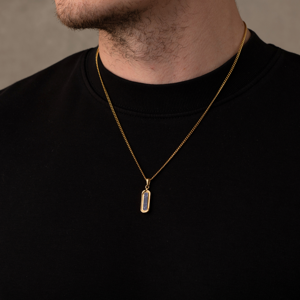 Gold necklace with a pendant on a person wearing a black shirt against a neutral background