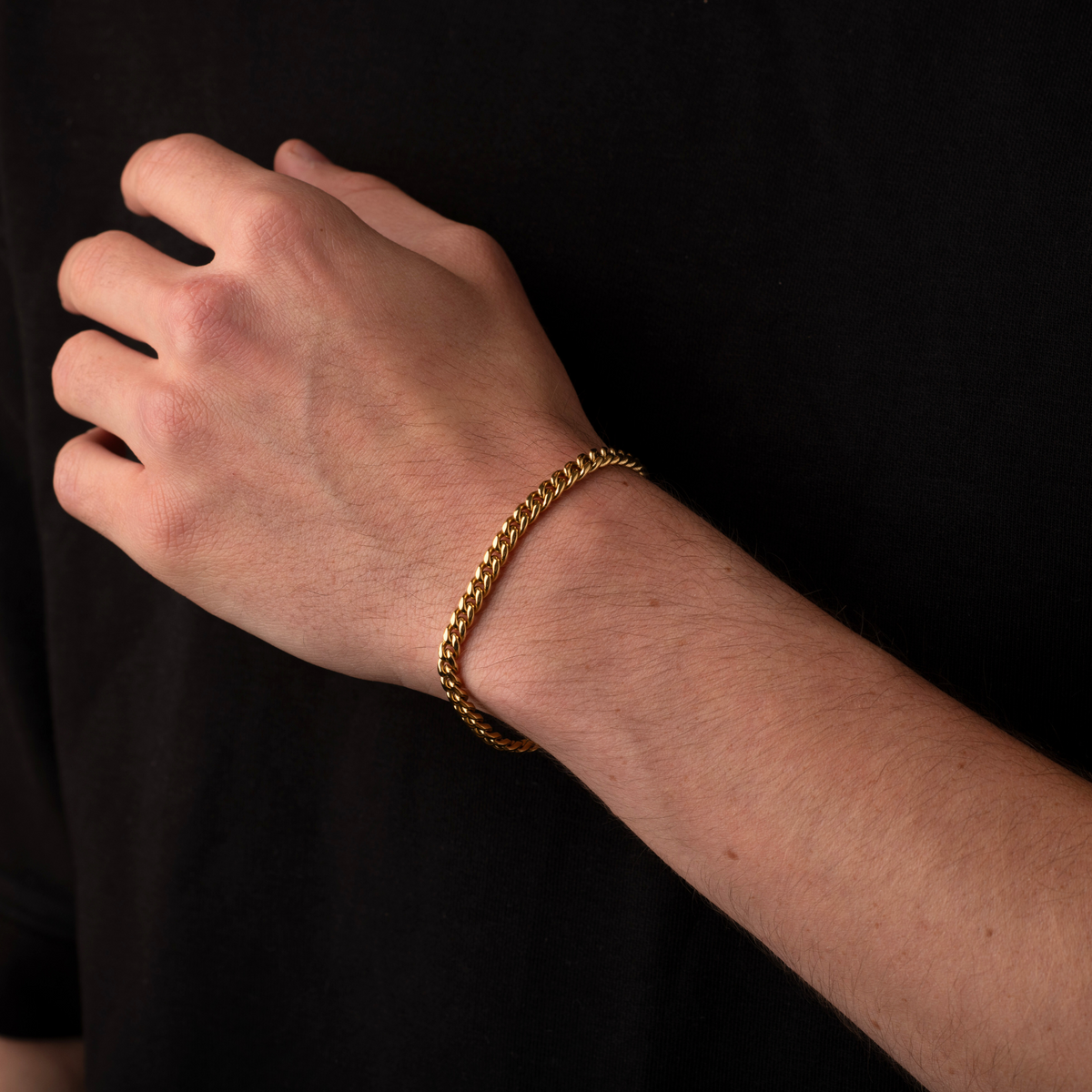 Hand wearing a gold bracelet against a black background