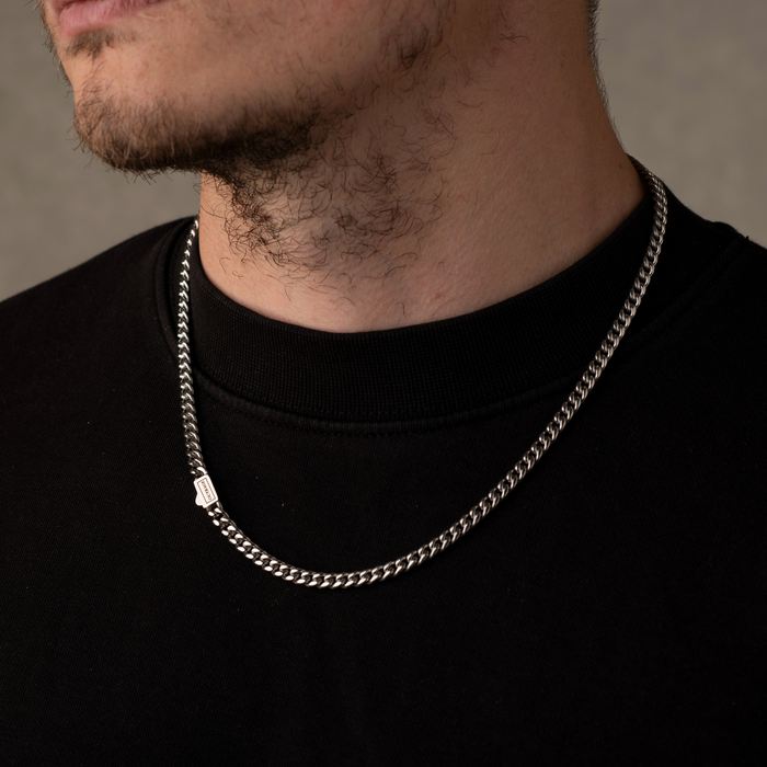 Silver chain necklace worn by a person against a neutral background