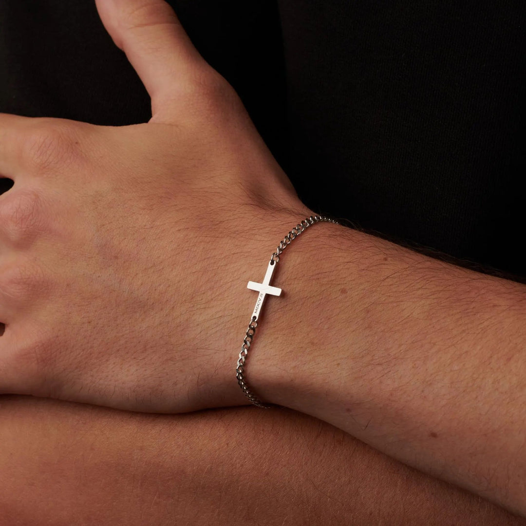 A close-up view of a person's wrist wearing a silver cross-shaped bracelet.