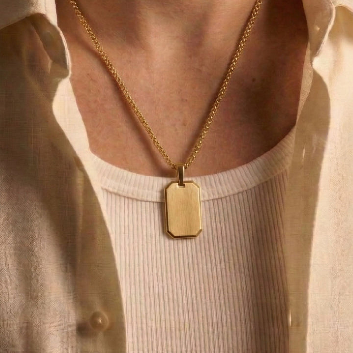 A gold chain necklace with a rectangular pendant is worn around a person's neck.