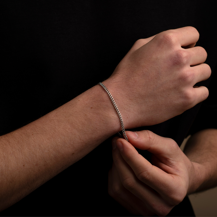 Person adjusting a silver bracelet on their wrist against a black background