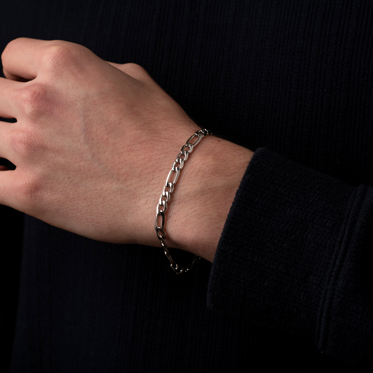 Hand wearing a silver chain bracelet against a black background