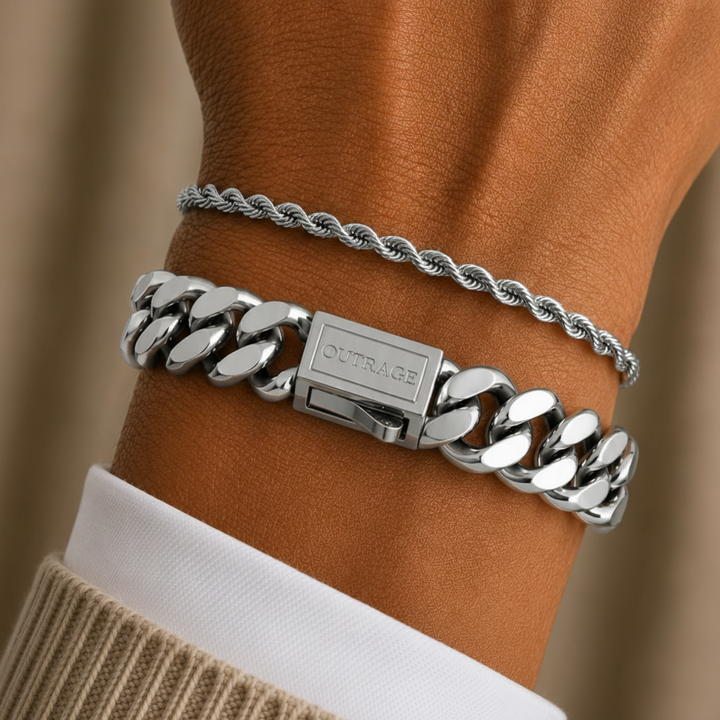 A close-up of a person's wrist wearing two silver bracelets: a thicker curb-link chain bracelet and a thinner twisted rope bracelet, layered over a white collared shirt and beige sweater.