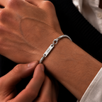 A close-up of a person's wrist wearing a silver snake chain bracelet with a rectangular engraved plate that reads 'JAZ'.