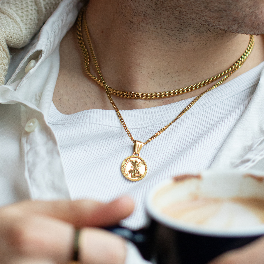 Person wearing a gold necklace with a pendant, holding a cup of coffee.