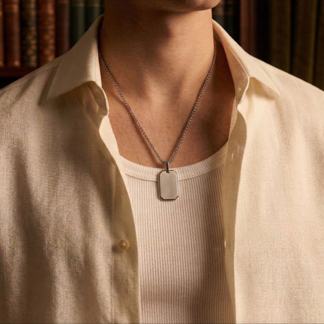 A close-up of a person wearing a white shirt and a silver necklace with a rectangular pendant.