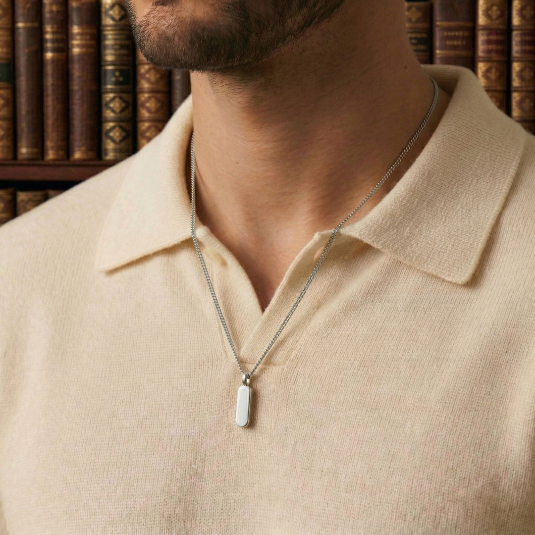 A close-up of a man wearing a cream-colored shirt and a silver necklace with a pendant.