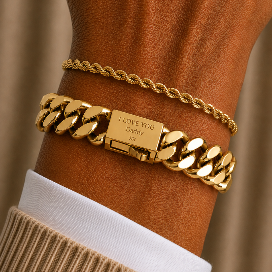 A close-up of a person's wrist wearing two gold bracelets: a thick curb-link chain bracelet engraved with 'I LOVE YOU Lady' and a thinner rope-style chain bracelet, layered over a white collared shirt and beige knit sweater cuff.