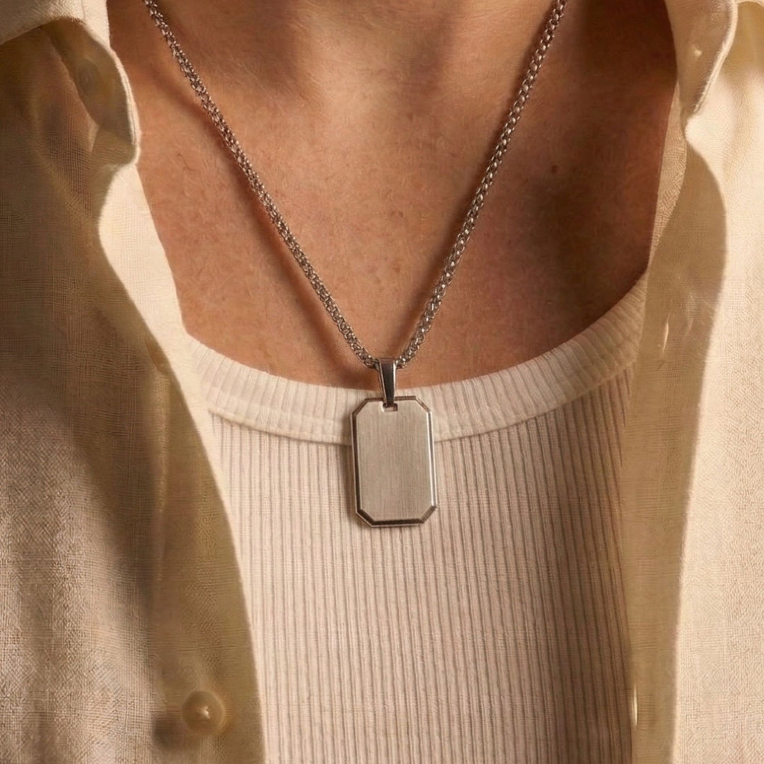A silver chain necklace with a rectangular pendant is worn around a person's neck.