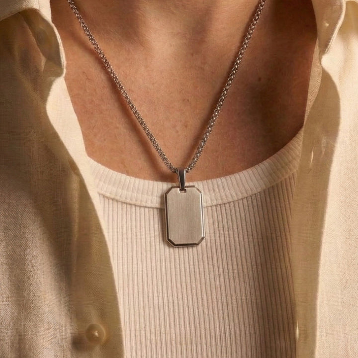 A silver chain necklace with a rectangular pendant is worn around a person's neck.