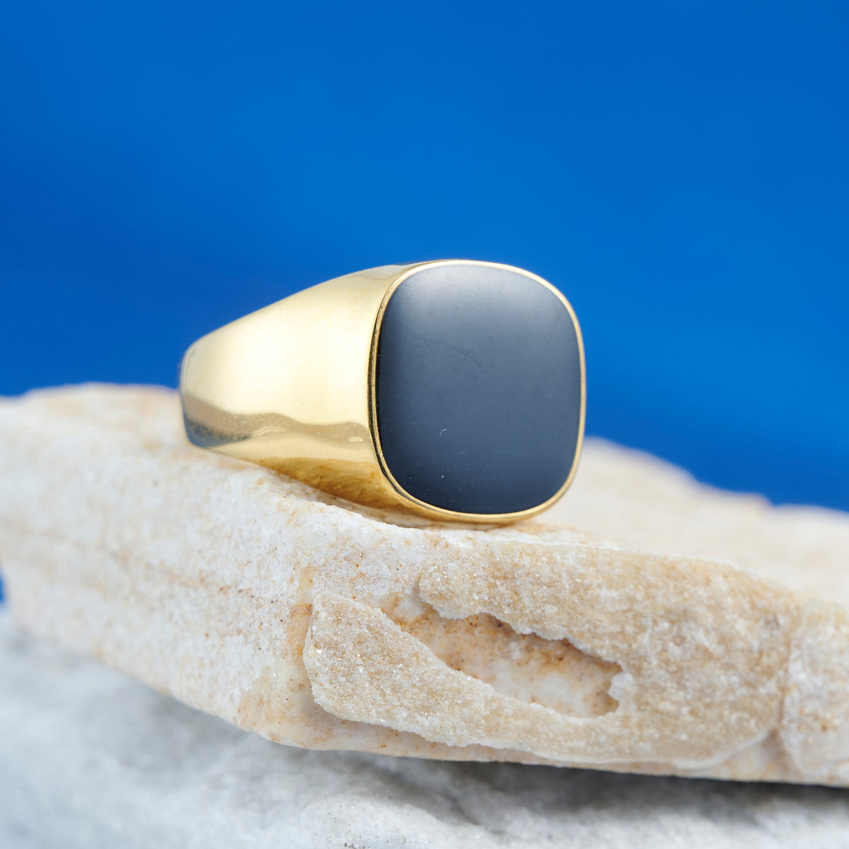 Gold ring with a black stone on a rock against a blue background