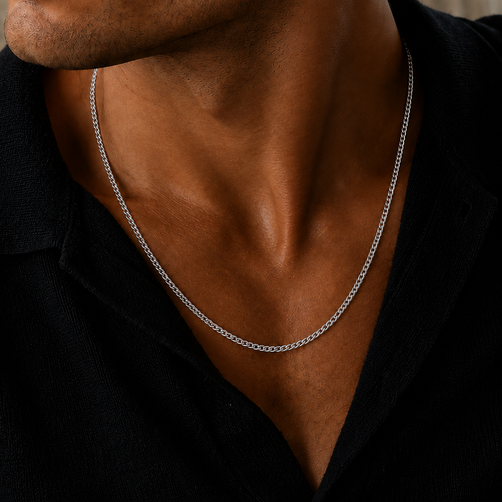 A close-up of a man's neck and chest wearing a silver chain necklace over a black shirt.