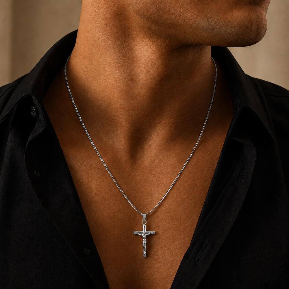 A silver crucifix pendant necklace worn by a man in a black shirt, shown in a close-up lifestyle shot.