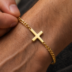 A gold cross bracelet is worn on a person's wrist.
