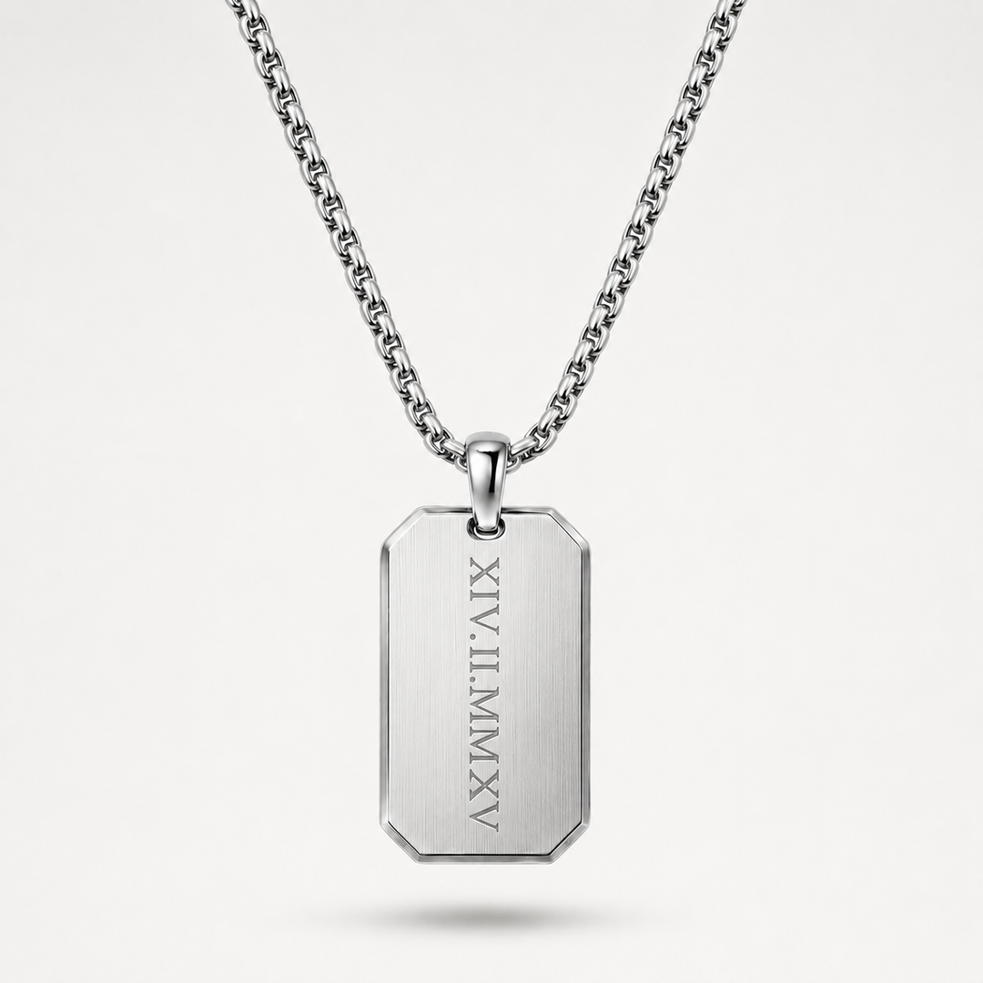 A silver-toned stainless steel dog tag necklace with a rectangular pendant engraved with vertical Roman numerals, suspended from a matching chain against a light gray background.