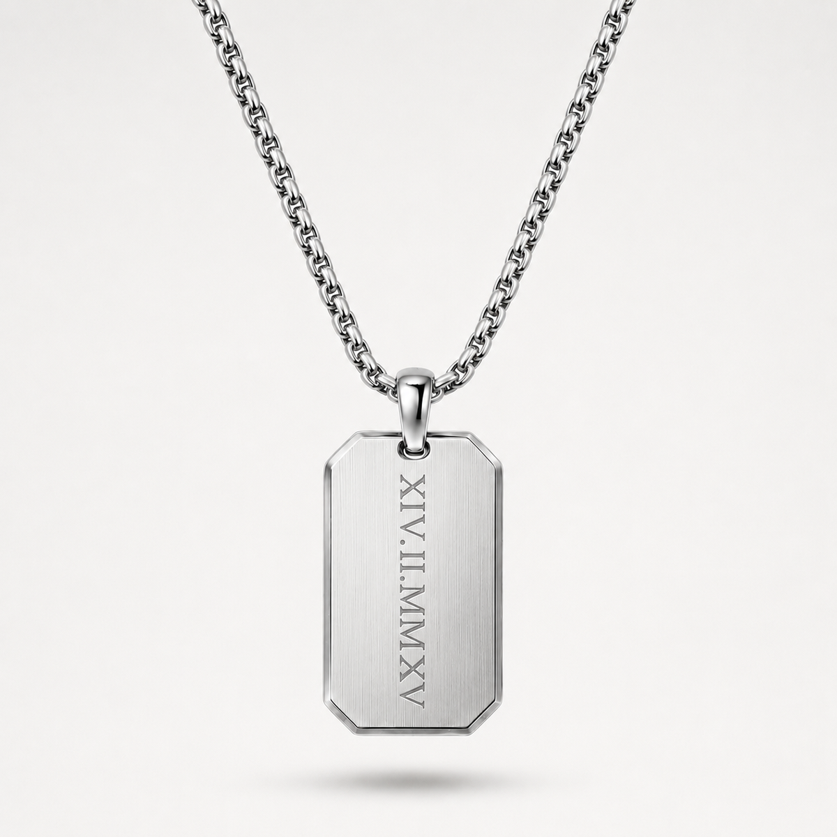A silver-toned stainless steel dog tag necklace with a rectangular pendant engraved with vertical Roman numerals, suspended from a matching chain against a light gray background.