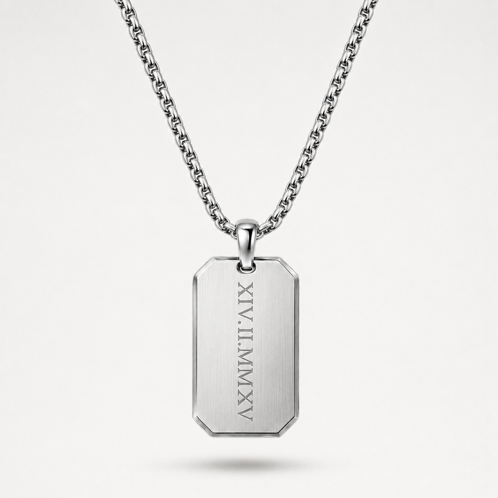 A silver-toned stainless steel dog tag necklace with a rectangular pendant engraved with vertical Roman numerals, suspended from a matching chain against a light gray background.