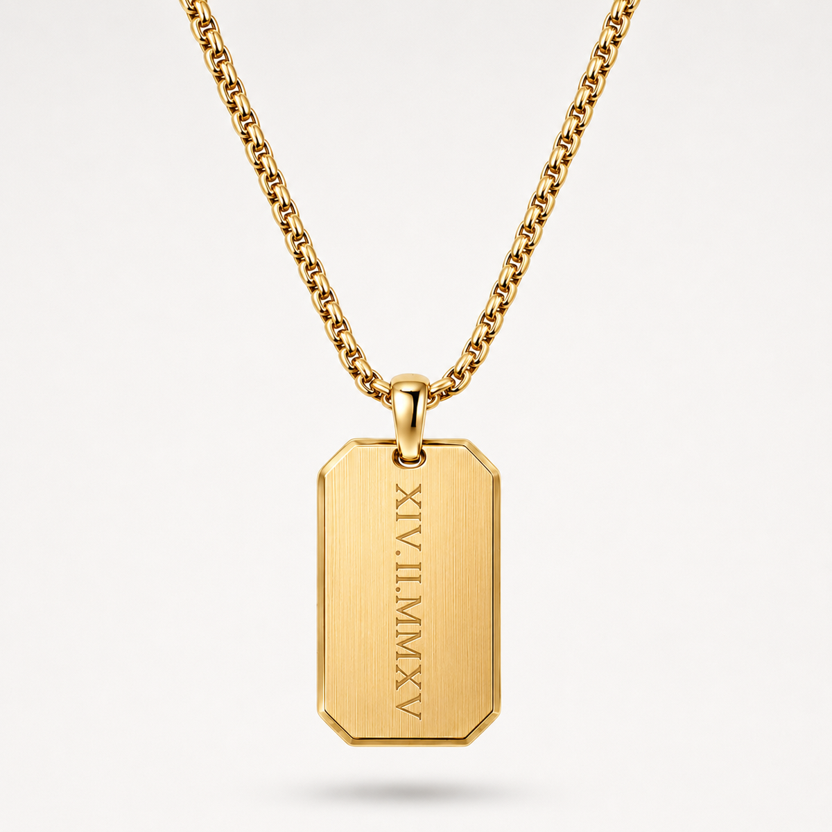 A gold-toned metal necklace with a rectangular dog tag pendant engraved with vertical Roman numerals, shown on a clean light gray background.