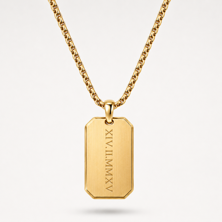 A gold-toned metal necklace with a rectangular dog tag pendant engraved with vertical Roman numerals, shown on a clean light gray background.