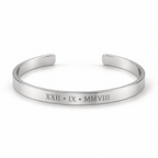 A polished silver cuff bracelet with Roman numerals engraved on the front, displayed on a clean white background.