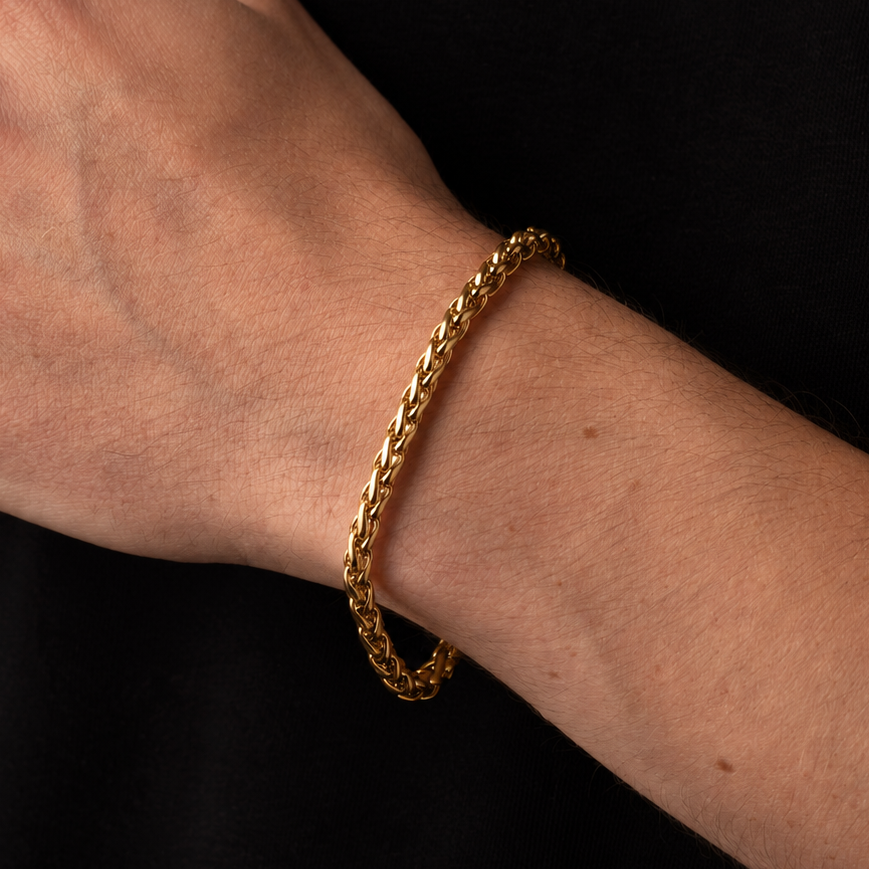 A close-up of a person's wrist wearing a gold braided chain bracelet against a black shirt background.