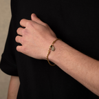 Hand wearing a gold bracelet with a dark background
