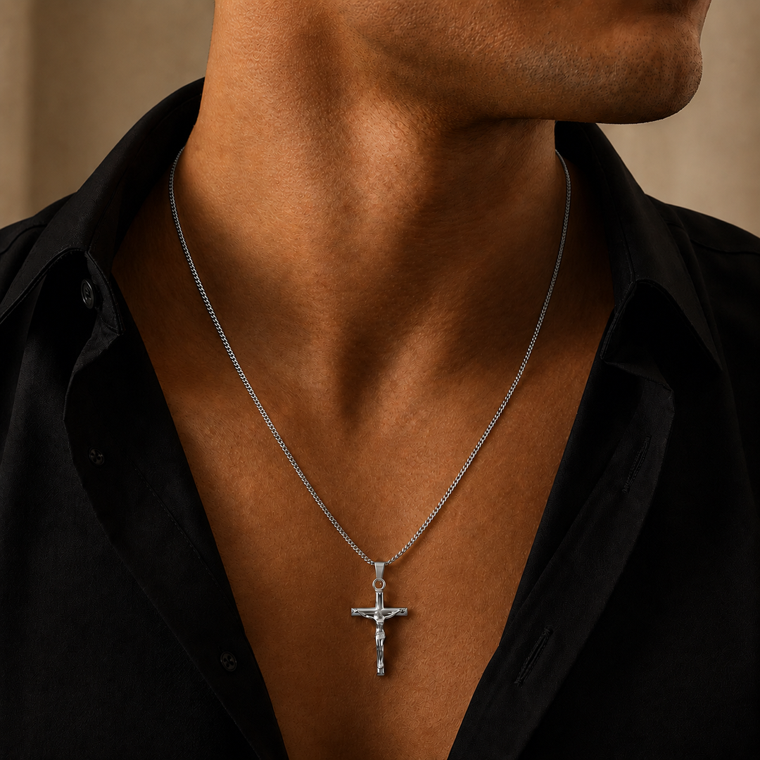 A silver crucifix pendant necklace worn by a man in a black shirt, shown in a close-up lifestyle shot.