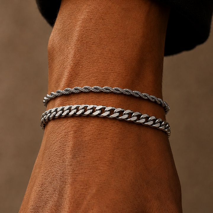 Two silver-toned bracelets, one twisted rope style and one curb link style, worn on a person's wrist against a warm brown background.