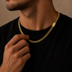 A close-up of a man wearing a gold Cuban link chain necklace with a rectangular engraved tag, paired with a black crewneck t-shirt against a warm beige background.