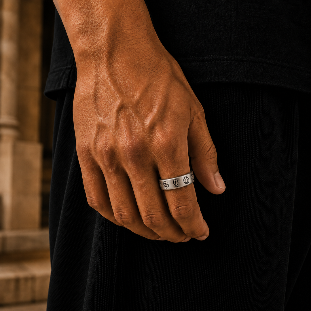 A close-up of a man's hand wearing a silver band ring with repeating interlocking circle motifs, set against a dark shirt and blurred stone background.
