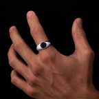 A silver-toned men's signet ring with a black oval inlay, shown worn on a person's ring finger against a solid black background.