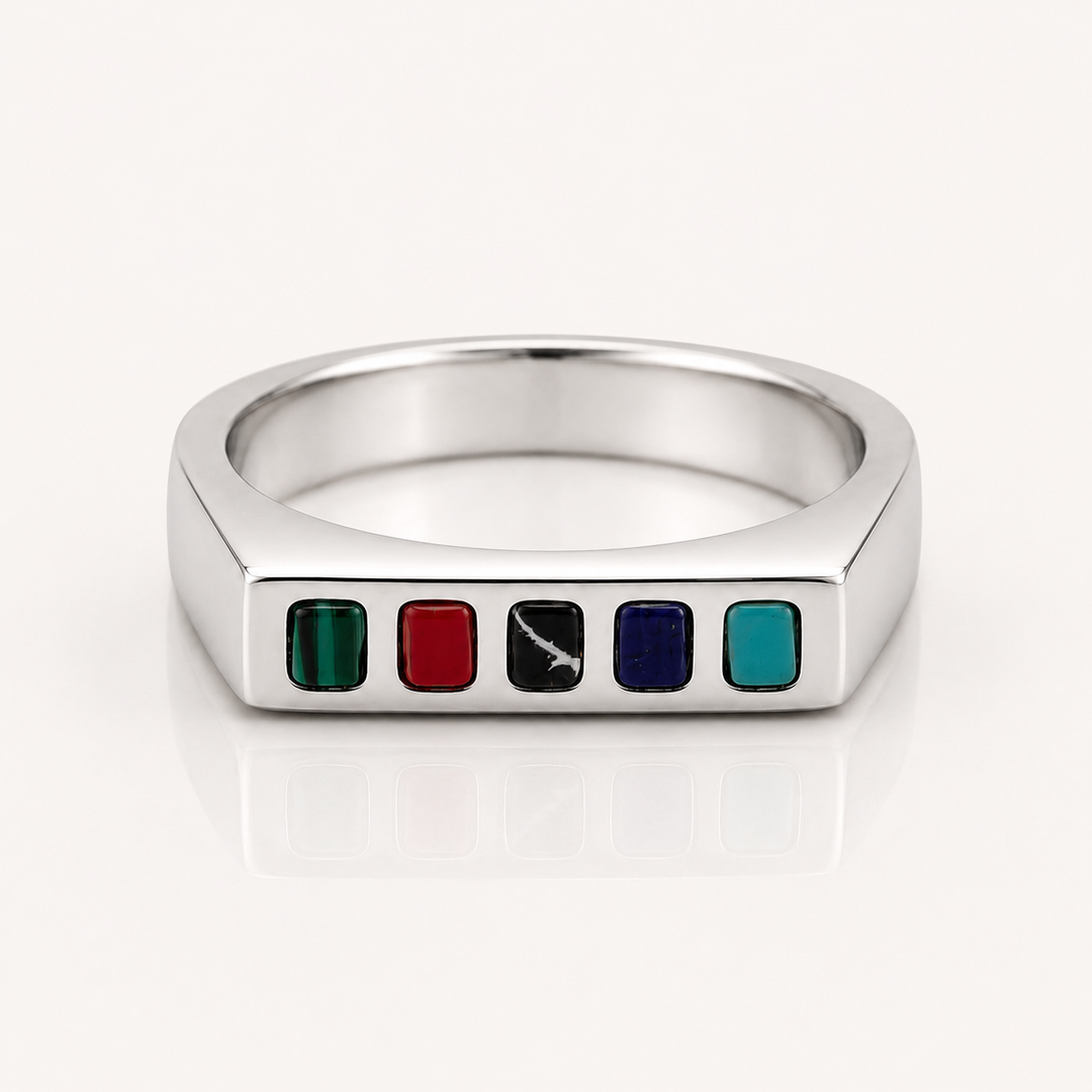 A silver-toned hexagonal ring featuring five small square enamel inserts in green, red, black, blue, and teal, set against a clean white background with a soft reflection.