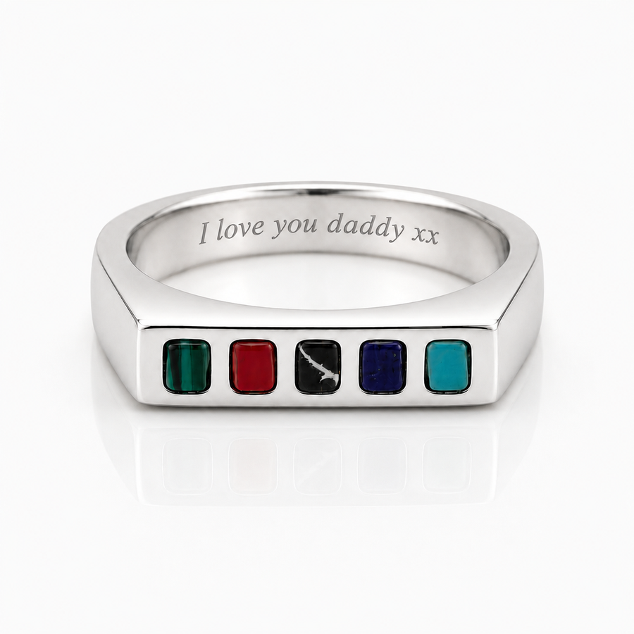 A silver-toned metal ring shaped like a tablet, featuring five small colored square inlays along the front edge: green, red, black with a white sword engraving, dark blue, and teal. The inside of the band is engraved with the text 'I love you daddy xx'.