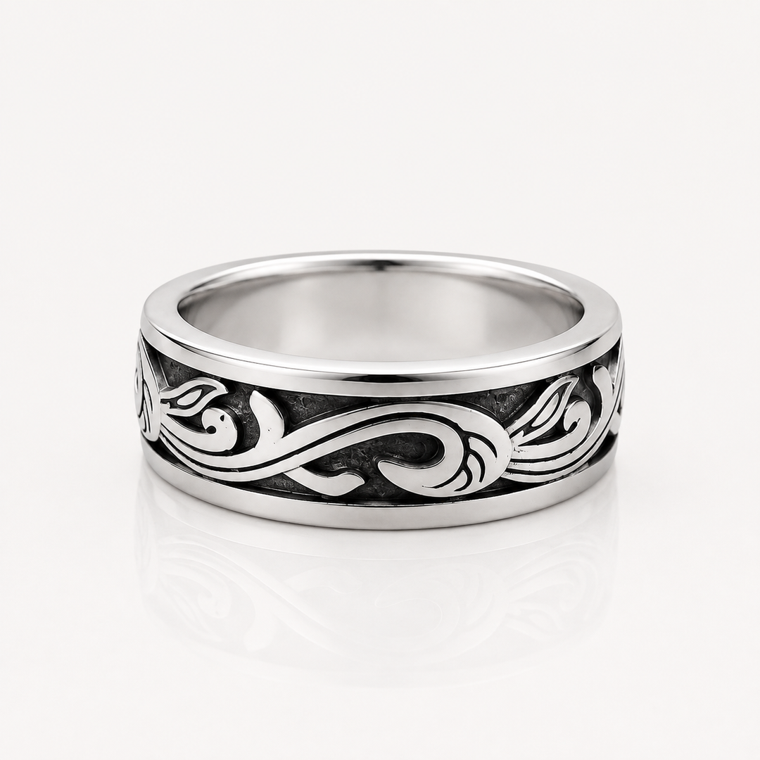 A silver band ring with a polished finish and an engraved black scrollwork pattern, shown on a clean white background with a soft reflection.