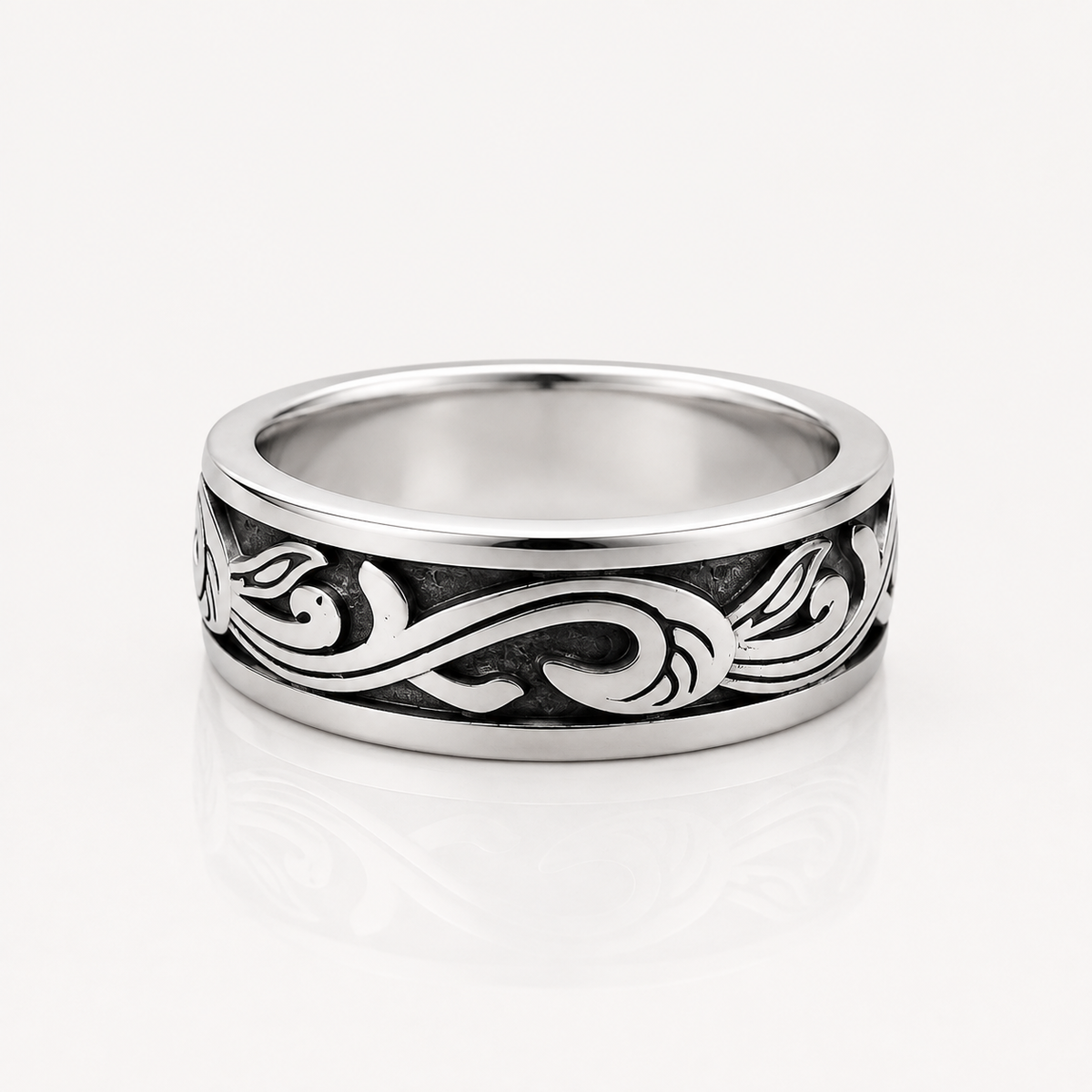 A silver band ring with a polished finish and an engraved black scrollwork pattern, shown on a clean white background with a soft reflection.